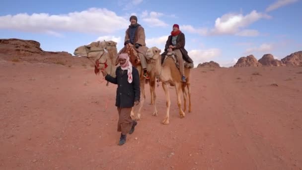 ワディ ジョーダン2020年1月19日 ワディ ラムの砂漠でラクダに乗っている若い女性と2人の男性の観光客 とても寒いので 彼女は伝統的なベドウィンコートを着ています ビスケット 地元の男がそれらをリード — ストック動画