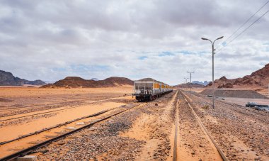 Wadi Rum tren istasyonundaki kullanılmayan eski tren kumlu çölün üzerindeki bulutlu gökyüzü.