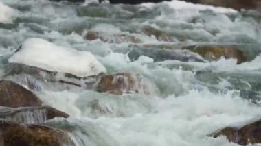 Kış nehri kar ve buzla kaplı taşların yakınından akıyor.