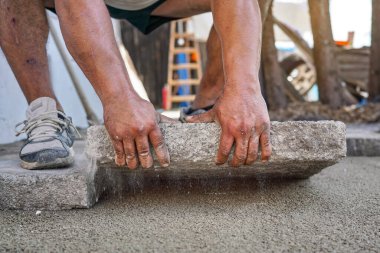 Büyük beton kiremitlerden yeni kaldırım ya da zemin döşeniyor. Taş bloğu kum ve çakıl taban katmanına sığdıran erkek işçilere yakın çekim detayları..