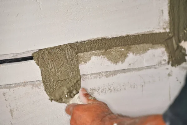 建筑工人用小铲子把电源插座槽固定在光秃秃的墙壁上 用砂浆水泥浆充填孔 — 图库照片