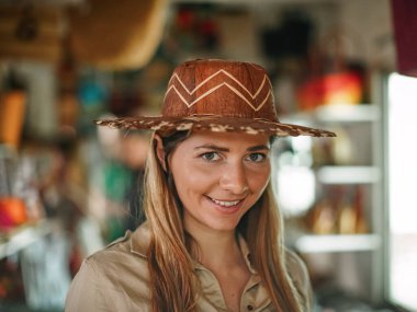 Afrika hediyelik eşya dükkanında hasır şapkayla poz veren genç bir kız, yakın plan portresi.