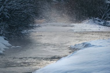 Soğuk kış nehri, suyun üstünde görünen buhar, her iki tarafta da koyu ağaçlar.