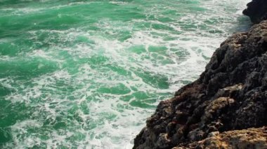 Kayalık kıyıya vuran deniz, sıçrayan yeşil su, yukarıdan görünen beyaz köpük, yavaş çekim videosu