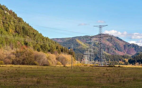 Kırsal kesimlerde inşa edilmiş büyük metal elektrik direği. Sonbahar çimenleri ve orman kaplı tepeler, mavi gökyüzü arka planı.