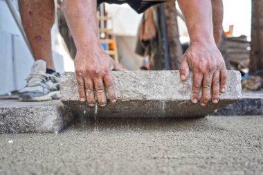 Büyük beton kiremitlerden yeni kaldırım ya da zemin döşeniyor. Taş bloğu kum ve çakıl taban katmanına sığdıran erkek işçilere yakın çekim detayları..