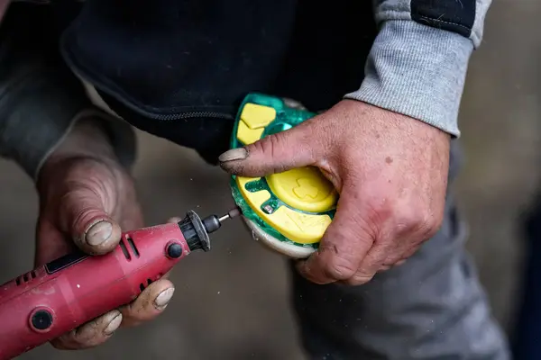 Man farrier installing plastic horseshoe to hoof. Closeup up detail to hands holding animal feet and rotary tool grinder.