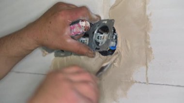 Erkek inşaat işçisi, çıplak duvara havan topu macunuyla elektrik prizleri yerleştiriyor. Delikleri sadece küçük kepçelerle dolduruyor.