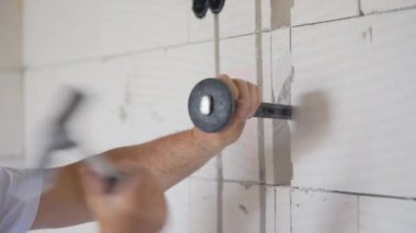 İnşaat işçisi elektrikli kablo takip kanallarını duvar keskisiyle genişletiyor. Detaylar elinde aleti tutuyor ve çekice vuruyor.