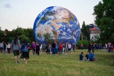 Brno, Çek Cumhuriyeti - 12 Temmuz 2020: Gezegen parkı yakınlarındaki yeşil çayır üzerinde şişme Dünya modelinin önünde yürüyen insanlar