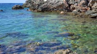 Yunanistan 'ın Korfu kentindeki Limni sahilinde kristal berrak deniz suyu, geniş yuvarlak taşlı deniz tabanı ve kıyı zemininde keskin kayalar