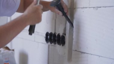İnşaat işçisi elektrikli kablo takip kanallarını duvar keskisiyle genişletiyor. Detaylar elinde aleti tutuyor ve çekice vuruyor.