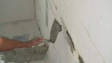 Erkek inşaat işçisi, duvar arkasından havan mermisiyle kovalamacaya elektrik kabloları yerleştiriyor. Delikleri küçük mason kepçesiyle dolduruyor. Detaylar sadece ellerde.