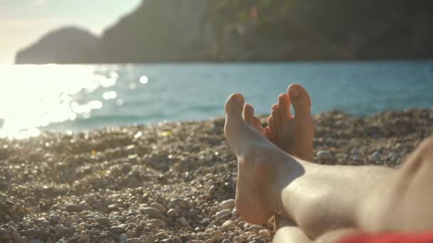 Młody Człowiek Odpoczywający Żwirowej Plaży Tylko Skrzyżowane Gołe Stopy Widoczne — Wideo stockowe