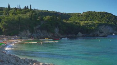 Liapades, Yunanistan - 19 Eylül 2022: Güneşli yaz sabahında Liapades Körfezi sahil iskelesinde tekne bekleyen insanlar, sakin bir deniz teknesi daha