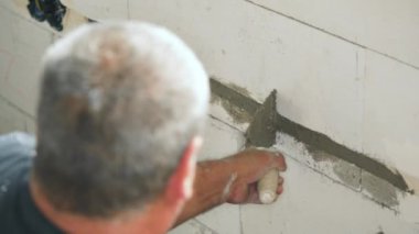 Erkek inşaat işçisi, duvar arkasından havan mermisiyle kovalamacaya elektrik kabloları yerleştiriyor. Delikleri küçük mason kepçesiyle dolduruyor. Detaylar sadece ellerde.