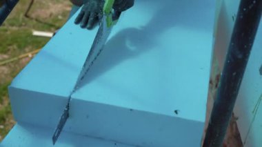 Adamın biri el testeresi ile polistiren köpük ısı yalıtımı kesiyor. Her şey mavi çünkü yanında renkli koruyucu folyo var.