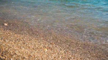 Pürüzlü kumsal, güneşle aydınlanan deniz suyu kıyıya vurur, yakın plan detayları- tropikal tatil arka planının sığ derinliği