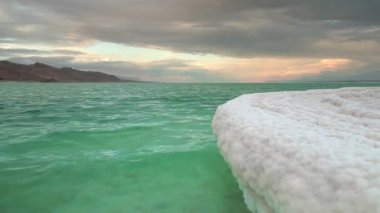 Tamamen kristal tuza bulanmış kum, Ölü Deniz kıyısında kar veya buz gibi görünüyor, turkuaz yeşil su, sabah güneşiyle boyanmış gökyüzü - Ein Bokek kumsalında manzara, İsrail