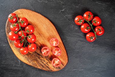 Tahta kesme tahtasında taze kırmızı kiraz domatesleri, biraz dilimlenmiş siyah tahta üzerinde masa gibi