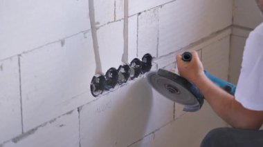 Erkek inşaat işçisi beton duvardaki elektrik kablolarını kovalıyor. Elektrikli taş testereli, havadan görülebilen toz.