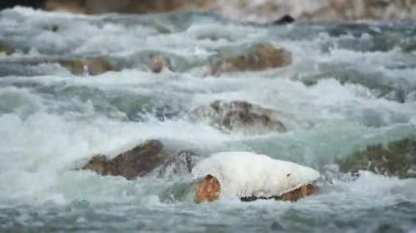 Kış nehri kar ve buzla kaplı taşların üzerinde akıyor.