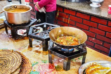 Tipik Pakistan restoranındaki basit gaz ocaklarında hazırlanan yiyecekler, sıcak tabak ve yakın çekim detaylarıyla çelik tavaya dökülen bitkiler ve baharatlar