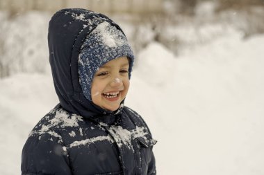 Tatlı gülümseyen karlı çocuk kış mevsiminin tadını çıkarıyor.