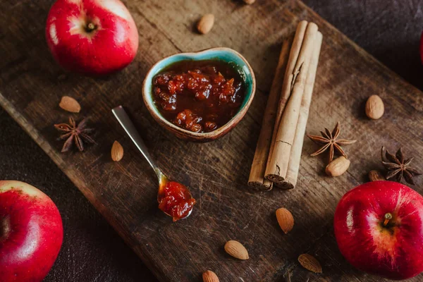 apple jam in a bowl, fresh fruits, apples, spicy spices of cinnamon, almond and anise on a brown wooden background