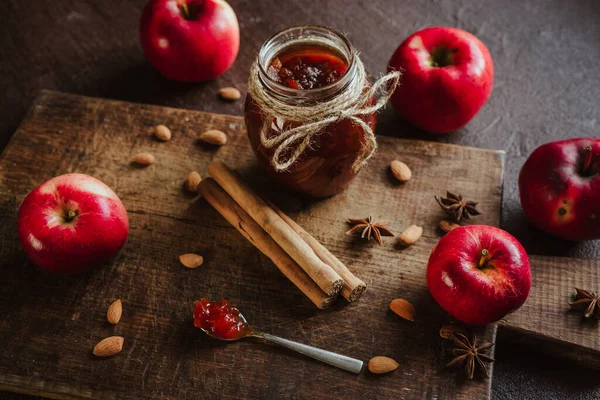 apple jam in a jar, fresh fruits, apples, spicy spices of cinnamon, almond and anise on a brown wooden background