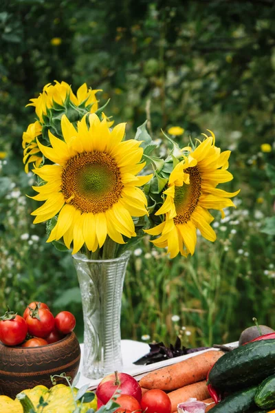 a bouquet of sunflowers on a table with an autumn harvest of vegetables and fruits on a natural green background