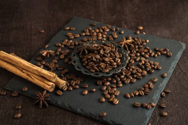 Baharatlı kavrulmuş kahve çekirdekleri, anason ve tarçın çubukları siyah arka planda metal bir Türk kasesinde.