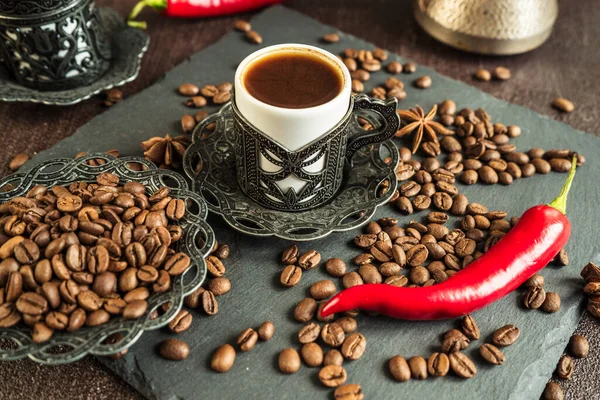 traditional turkish coffee in vintage cup, anise, roasted beans with hot spicy chili pepper on brown background