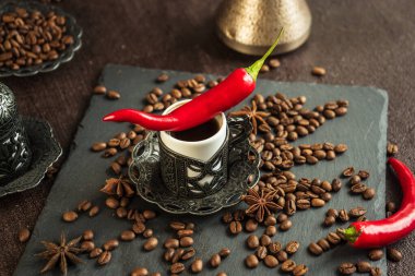 Klasik fincanda geleneksel Türk kahvesi, anason, kavrulmuş fasulye ve kahverengi arka planda acı biber.
