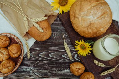 homemade wheat bread, freshly buns, mug with farm milk, sunflower, baked goods on brown wooden background 1