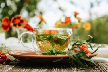 herbal tea of mint, calendula and sea buckthorn berries in a glass transparent cup on a brown wooden table. Alternative medicine