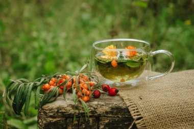 herbal tea of mint, calendula and sea buckthorn berries in a glass transparent cup on a brown wooden table. Alternative medicine