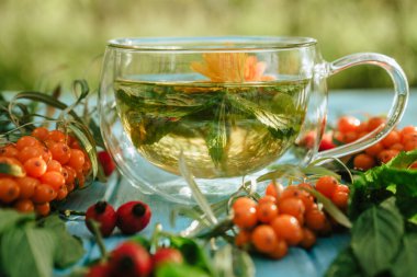herbal tea of mint, calendula, sea buckthorn berries and rose hips in a glass transparent cup on a blue wooden table