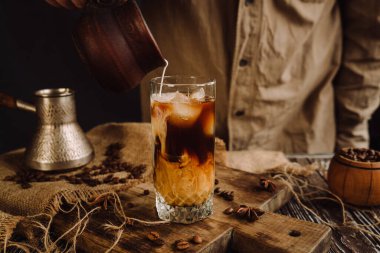 male barista pouring cream or milk into a glass of iced coffee 
