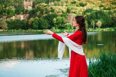 Vintage portrait of a beautiful noble lady in a red dress near the river. Historical reconstruction of the Victorian era.