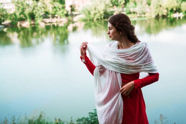 Vintage portrait of a beautiful noble lady in a red dress near the river. Historical reconstruction of the Victorian era.