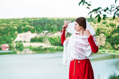 Vintage portrait of a beautiful noble lady in a red dress near the river. Historical reconstruction of the Victorian era.