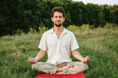 a young man doing yoga in nature with a smile, sitting in the lotus position 1