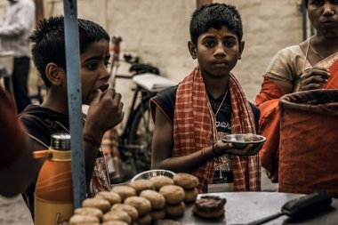 Rishikesh, 2017, annesi ve kardeşiyle Hintli çocuk panayırda sokak yemeği yiyor, köy pazarında.