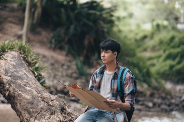 Sırt çantalı bir yürüyüşçü ormanda nehrin yanında yol tarifi bulmak için haritasını çıkarmış. yürüyüş ve macera konsepti.