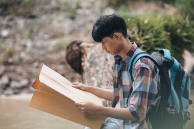 Sırt çantalı bir yürüyüşçü ormanda nehrin yanında yol tarifi bulmak için haritasını çıkarmış. yürüyüş ve macera konsepti.