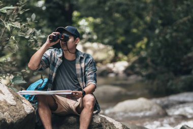 Yürüyüşçü elindeki haritaya bakıyordu ve ormandaki derenin oradaki yürüyüş yollarını bulmak için dürbünü kullanıyordu. yürüyüş ve macera konsepti