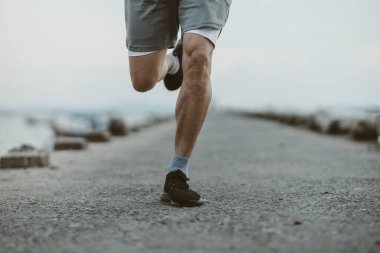 Sahil kenarındaki eski köprüde koşan sağlıklı yaşam tarzı genç bir fitness adamı. Açık hava sporu, sağlıklı yaşam tarzı konsepti.