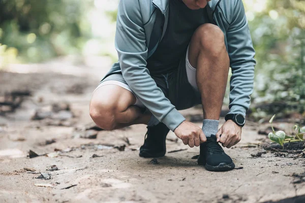 Sport man  tying jogging shoes in the forest. Outdoor workout,  Healthy lifestyle concept.