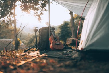 Kamp malzemeleri, çantalar, ayakkabılar, ukulele, sabahları çadırın yanında tripod. Nesne kampı, seyahat ve meslek kavramı.